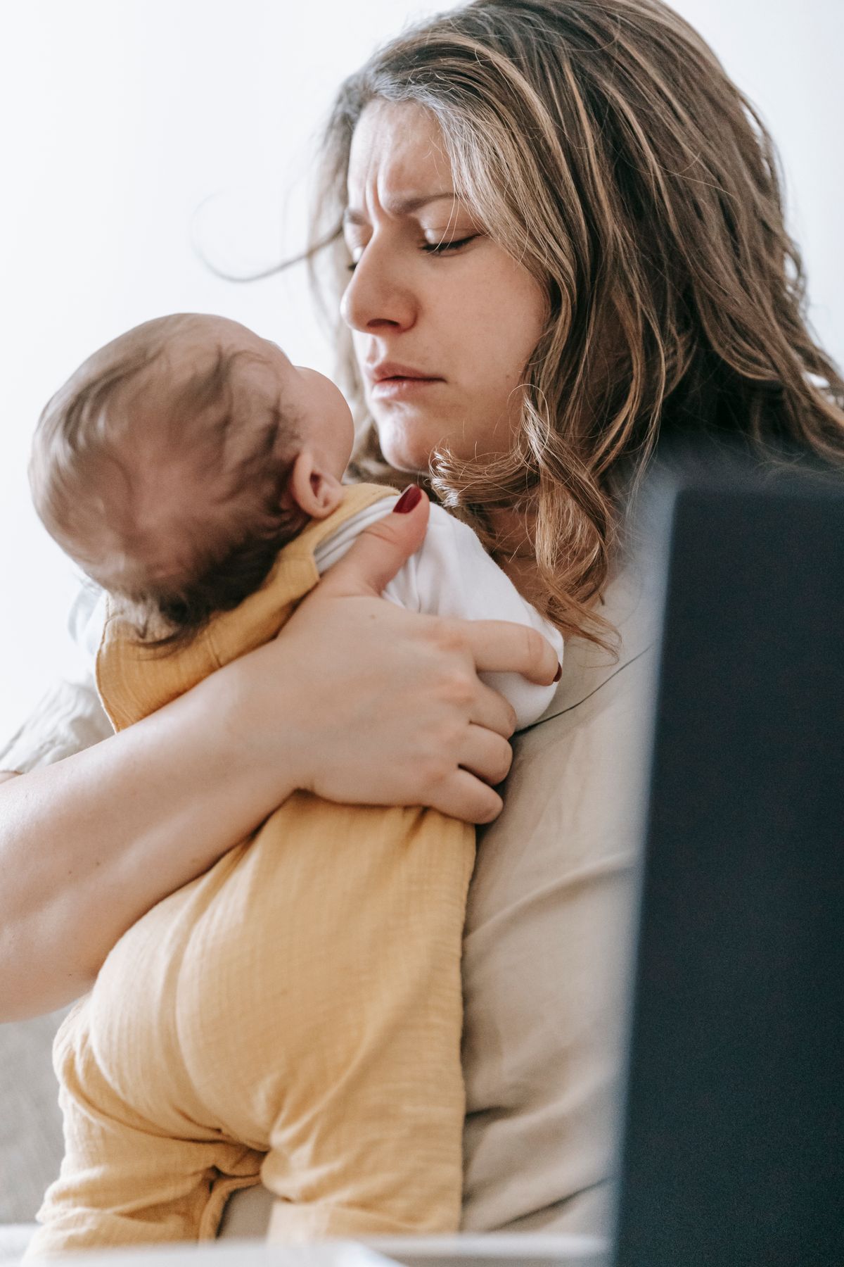 Mother comforting her infant while sitting near a laptop