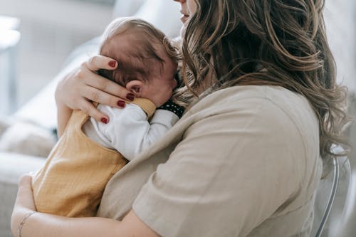 Free Side view of crop unrecognizable mum holding baby in arms in light room Stock Photo