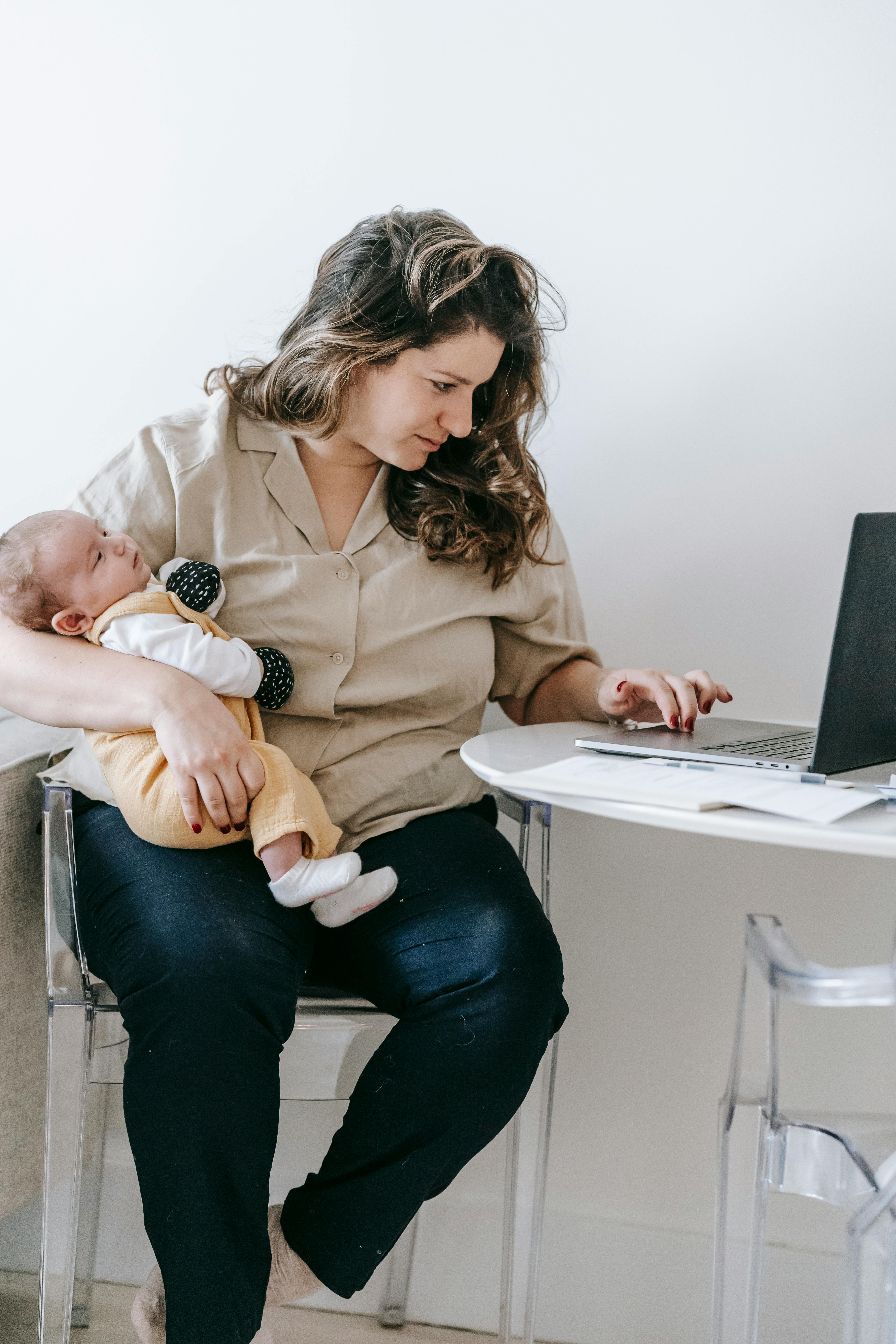 Cheerful young lady in sportswear holding boat pose with cute baby girl on  laps in modern apartment. Sporty adult mom doing baby yoga with little  daughter using online video on laptop at