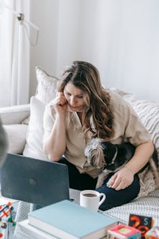 Focused woman working from home on laptop with her dog sitting on sofa.