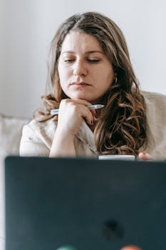 Focused woman in casual setting working on laptop from home, deep in thought.