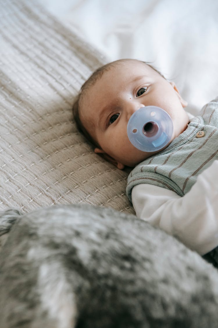 Newborn With Pacifier Lying On Bed