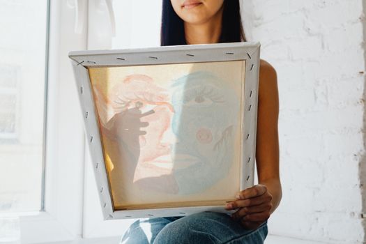 A woman holding and viewing a canvas painting in a bright, sunlit room, showcasing shadows.