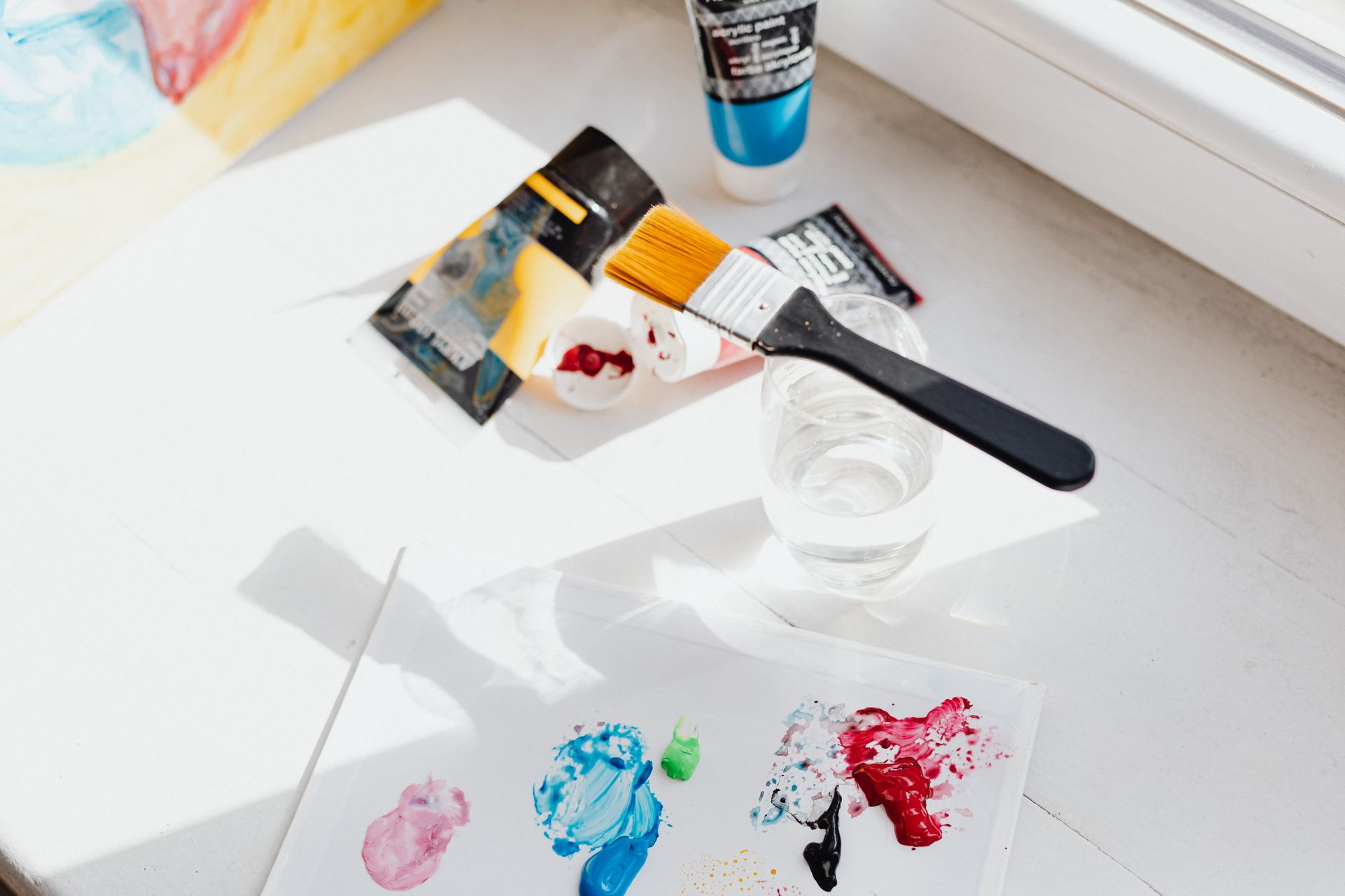 A bright overhead shot of art materials including paintbrushes and tubes on a white surface.