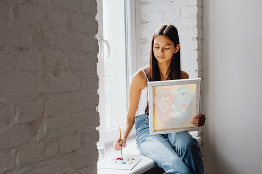 Teen girl painting at a sunlit window, expressing creativity and leisure.