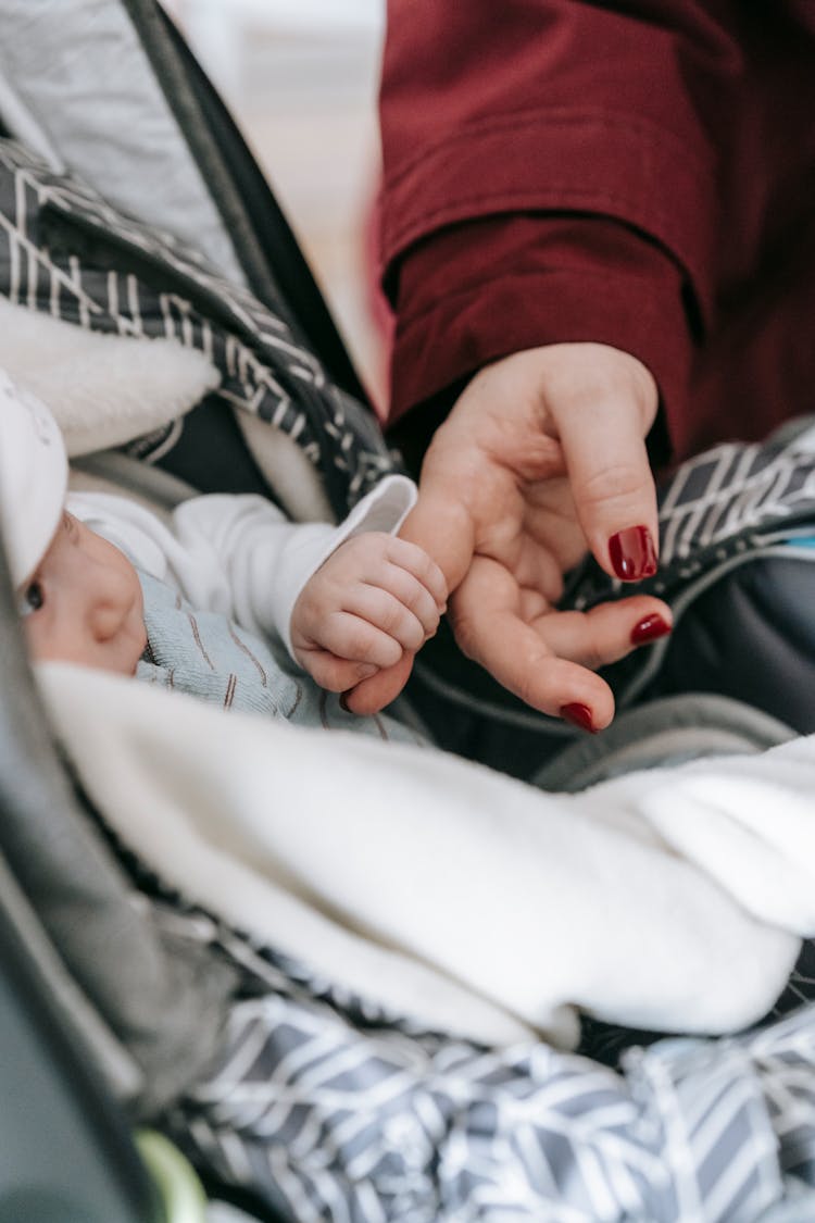 Adorable Infant In Stroller Holding Finger Of Crop Mom