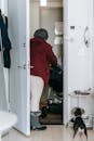 Back view of unrecognizable female in warm clothes entering apartment and leading baby stroller with dog standing near