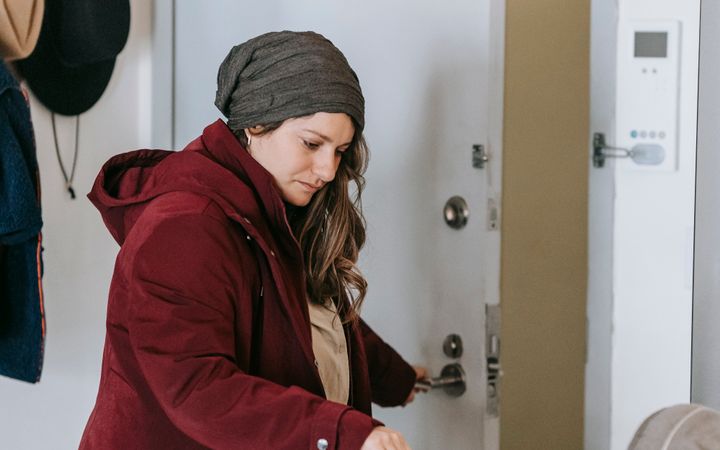Side view of concentrated mother in warm clothes looking at baby carriage while opening door and going for walk