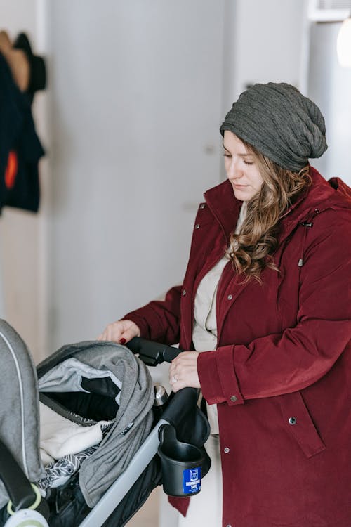 Free Side view of female in warm casual clothes with long hair looking at baby in stroller ready for walk Stock Photo