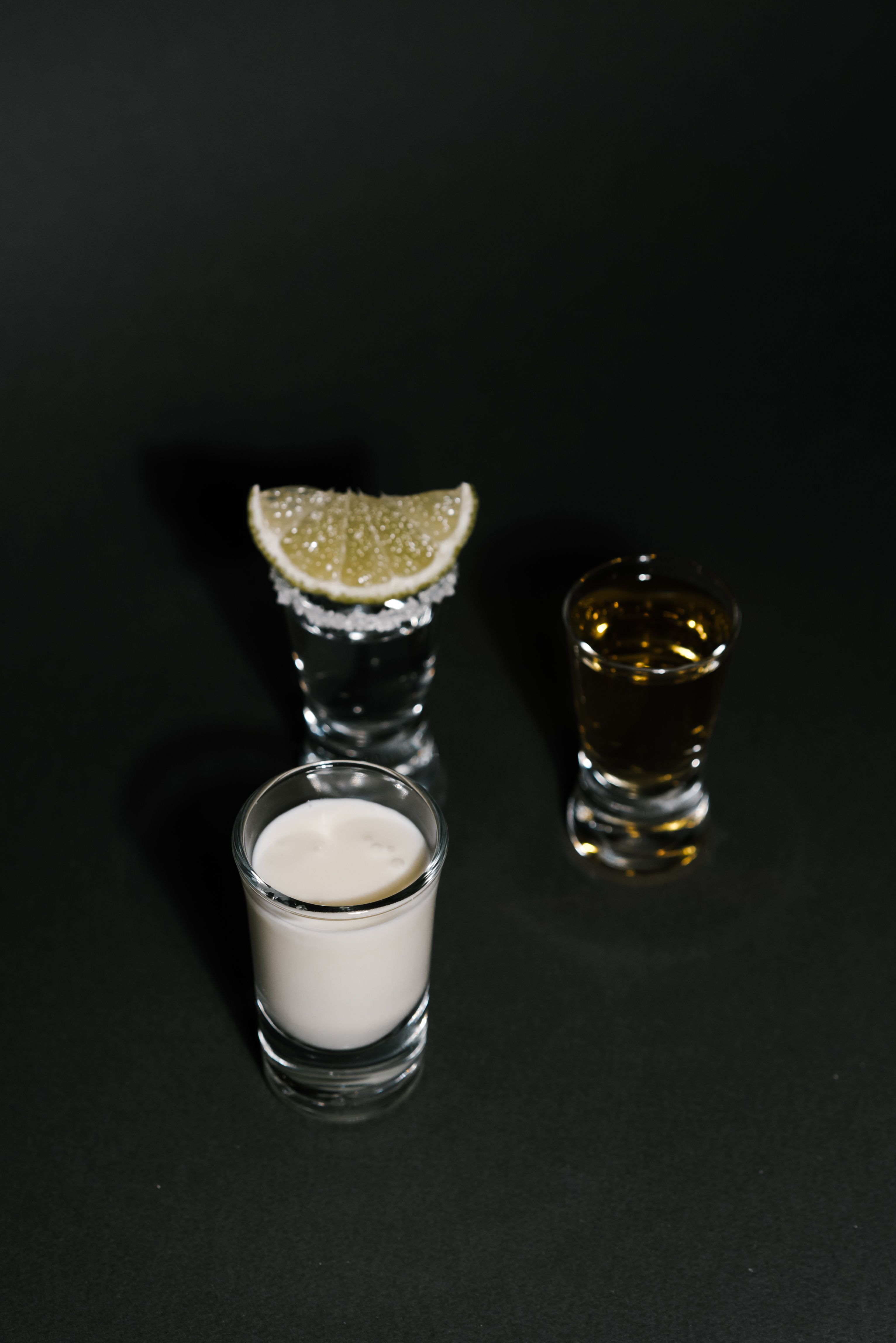 A trio of colorful cocktail shots paired with a lime wedge on a dark background.