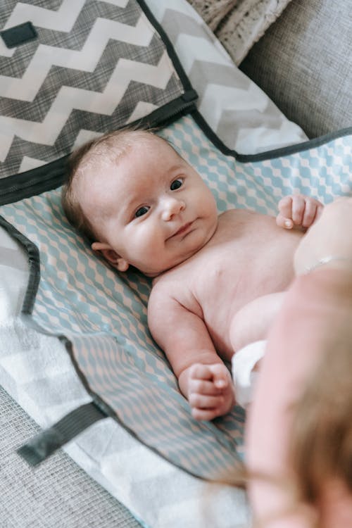 Free From above of crop unrecognizable parent near adorable infant baby in diaper lying on comfortable couch in light room in apartment Stock Photo