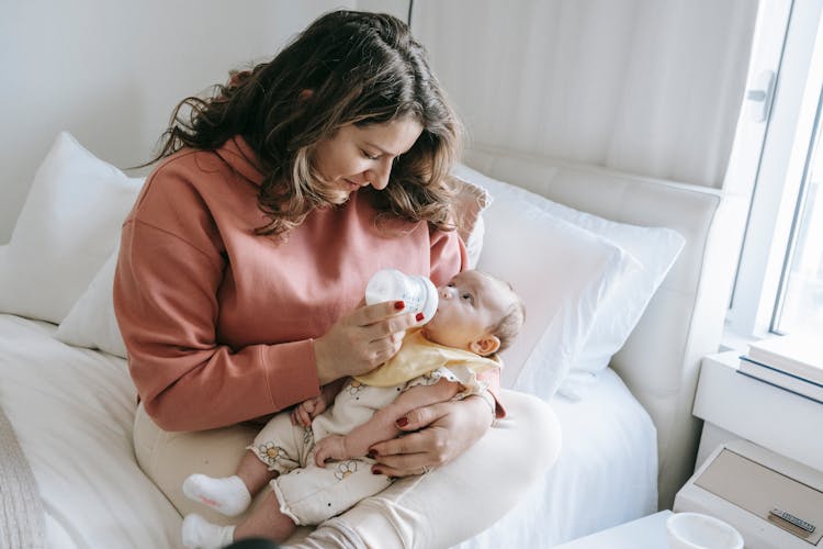 Mother Feeding Newborn Baby On Bed