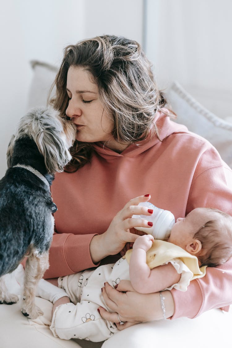 Mother Kissing Dog While Feeding Newborn Baby