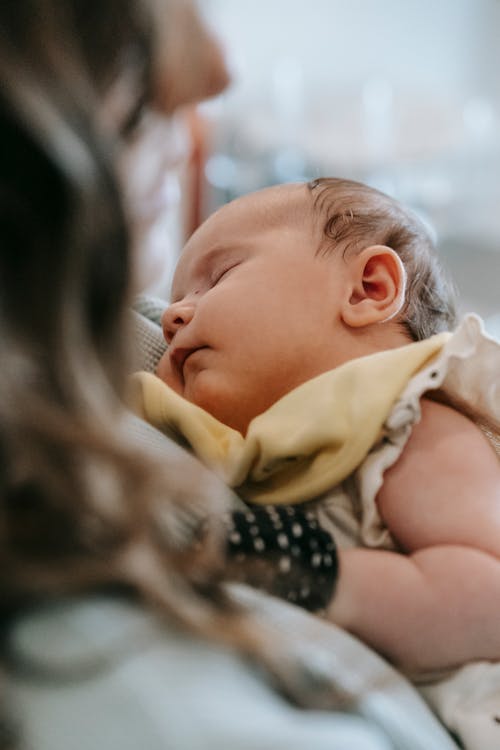 Cute baby sleeping in hands of crop mother