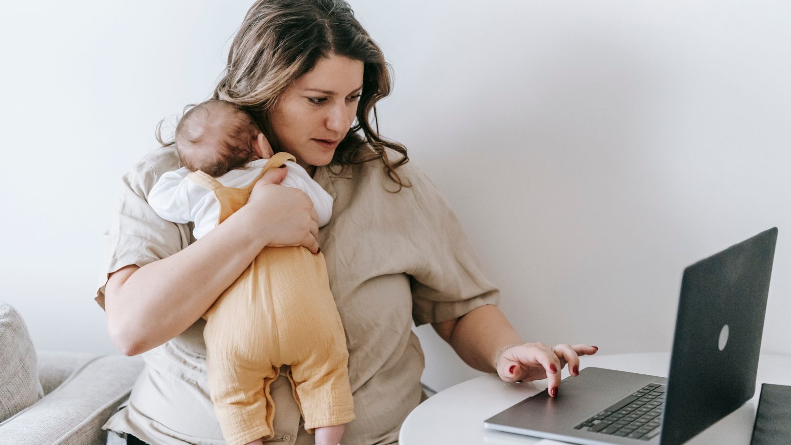 Mother holding her baby while checking her phone in a bright living room