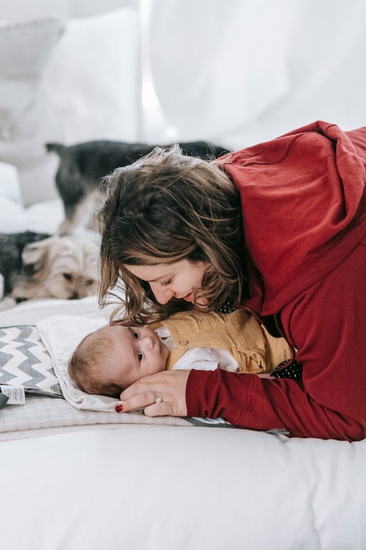 Smiling Young Mother Hugging Baby Lying On Bed