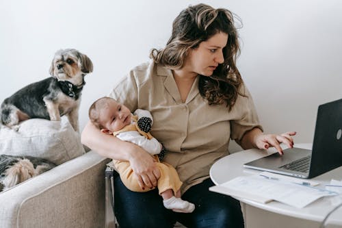 Woman Using Laptop while Carrying Her Baby