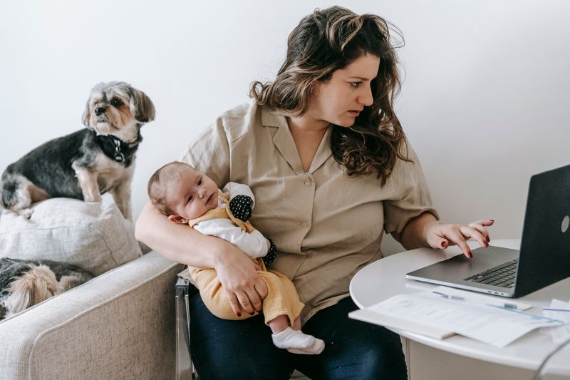Mutter hält ihr Baby im Arm und arbeitet am Laptop