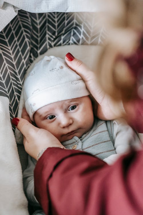 High angle of crop faceless mom putting hat on cute newborn lying in baby stroller before going to walk