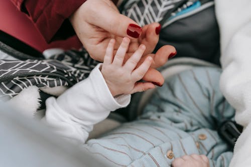 Crop faceless mom touching hand of newborn