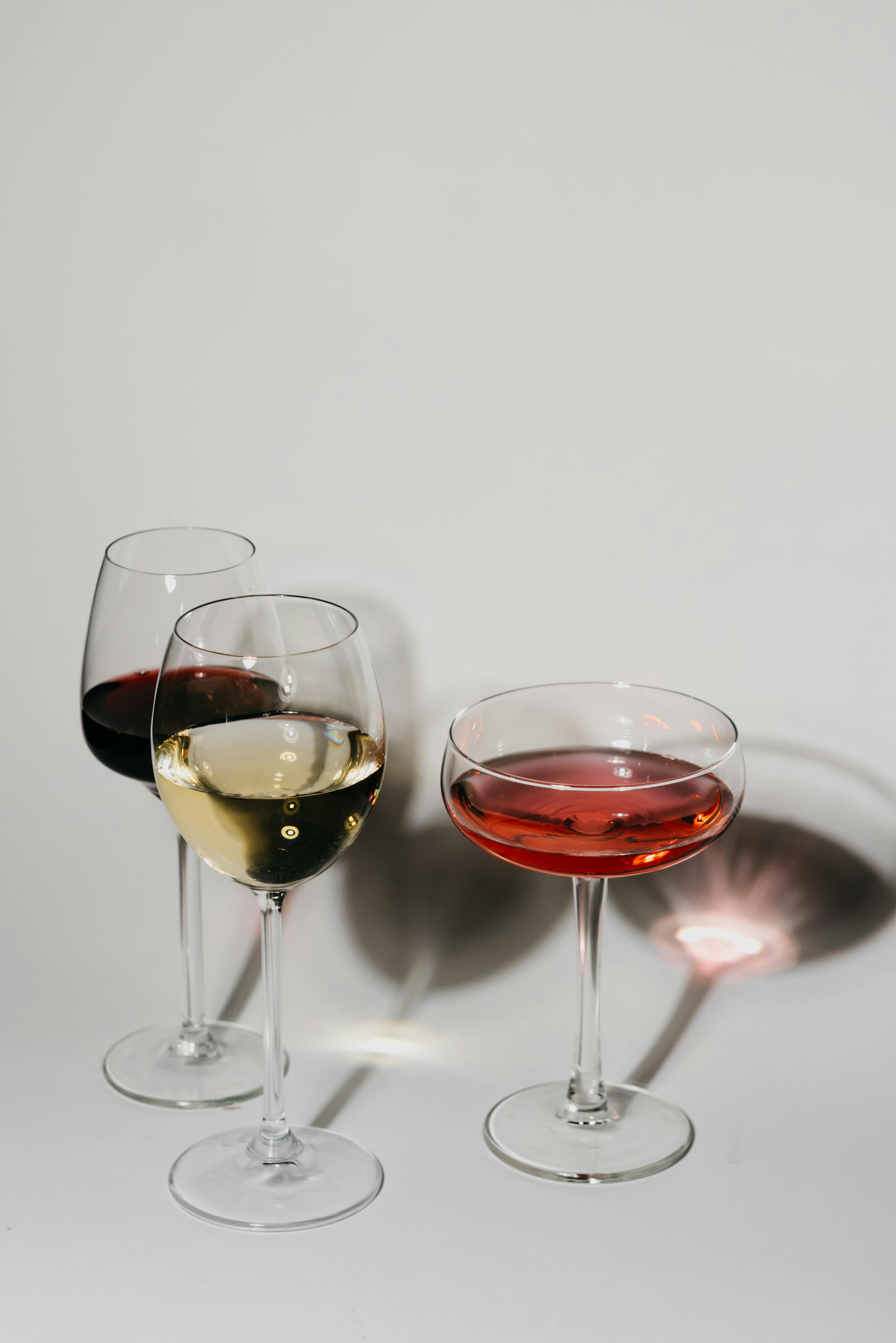 Three wine glasses on a flat surface showcasing red, white, and rosé wines with shadow play.