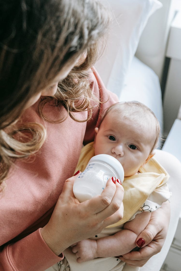 Cute Newborn Drinking Milk From Bottle In Hands Of Crop Mom