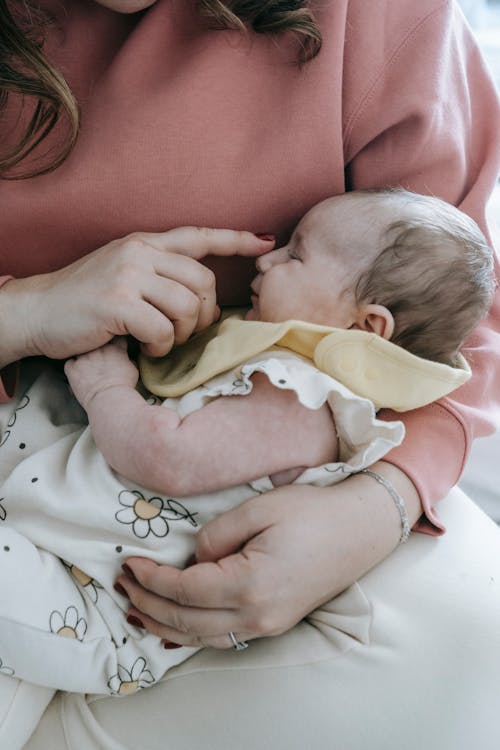 Crop mother touching nose of sleeping newborn