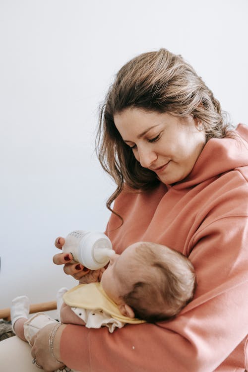 Delighted young mother embracing and feeding baby from bottle