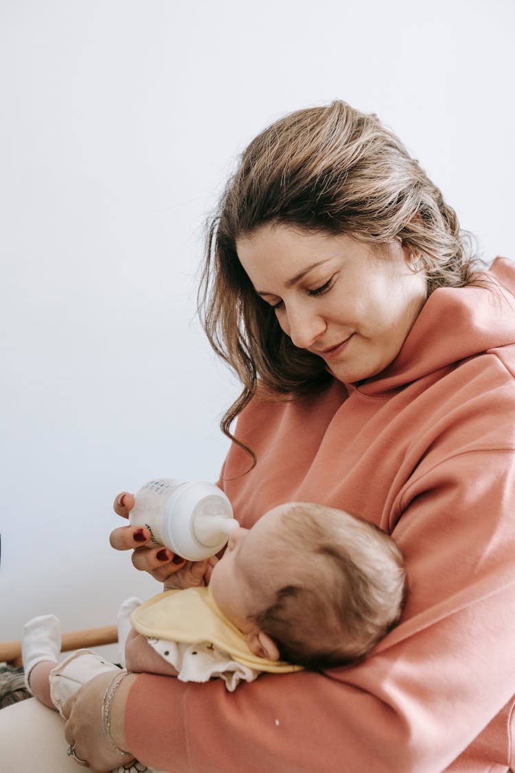 Delighted Young Mother Embracing And Feeding Baby From Bottle