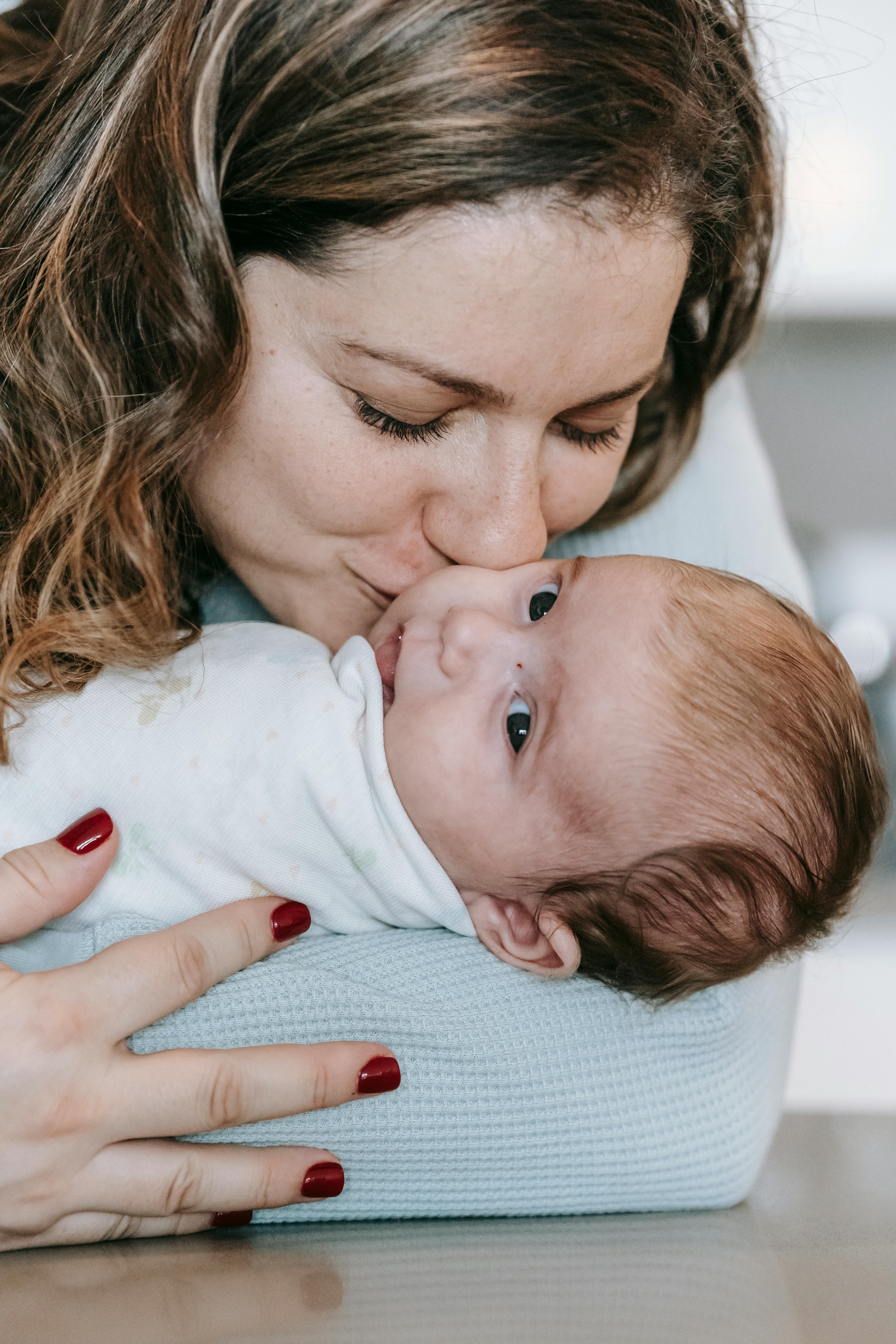 smiling mother kissing cute infant with closed eyes