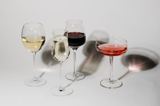 A close-up of various wine and champagne glasses on a white background casting shadows.