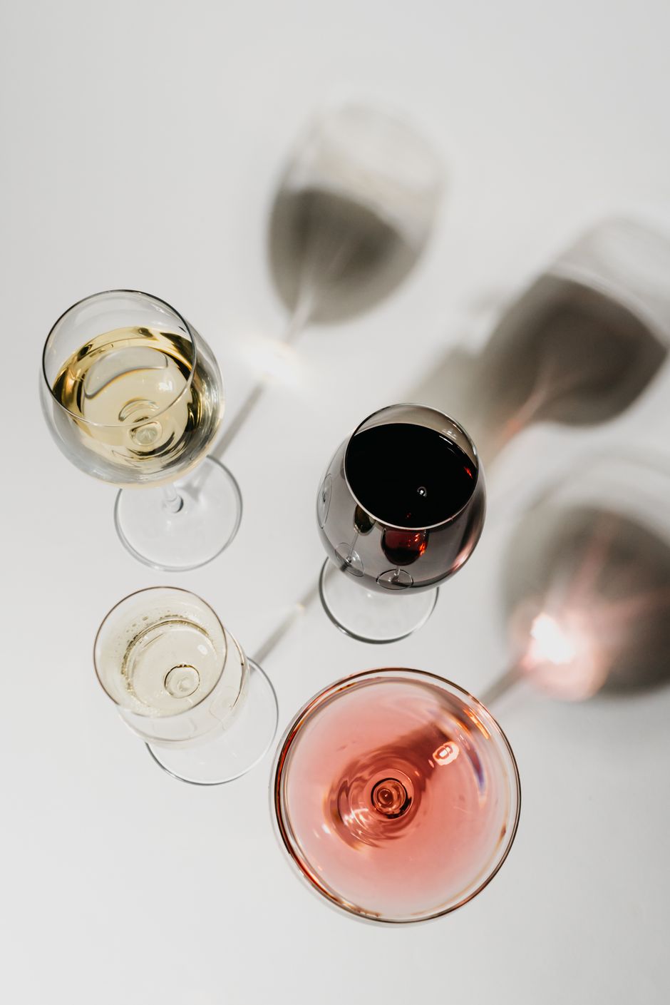 Aerial view of different wine glasses casting shadows on a white surface, showcasing a variety of wines.