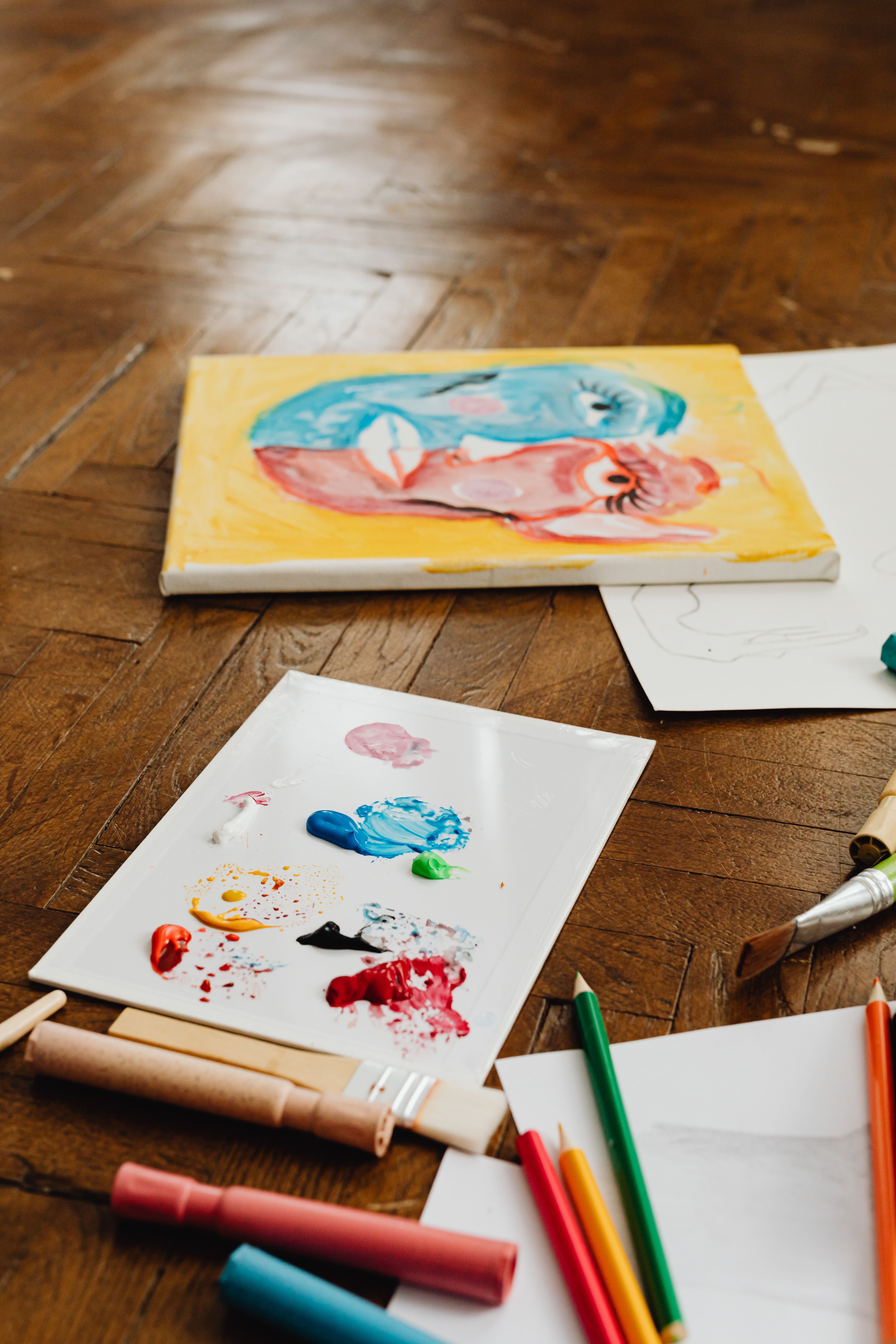 Art supplies and colorful painting on a wooden floor, showcasing creativity.