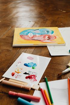 Art supplies and colorful painting on a wooden floor, showcasing creativity.