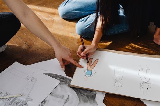 Close-up of hands sketching fashion designs on paper indoors.