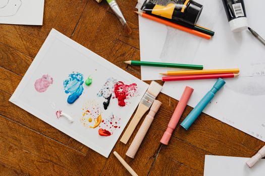 Flat lay of colorful art supplies including paints and pencils on a wooden floor for creative inspiration.