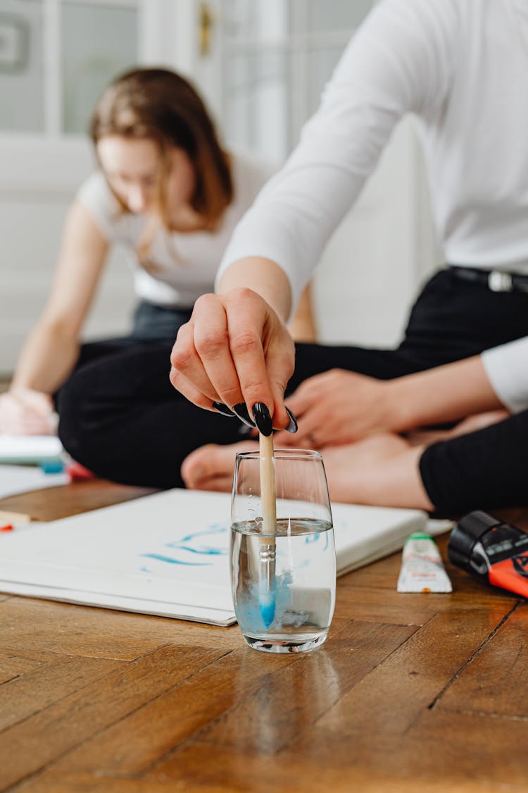 Female Hand Washing Paintbrush In Glass Of Water