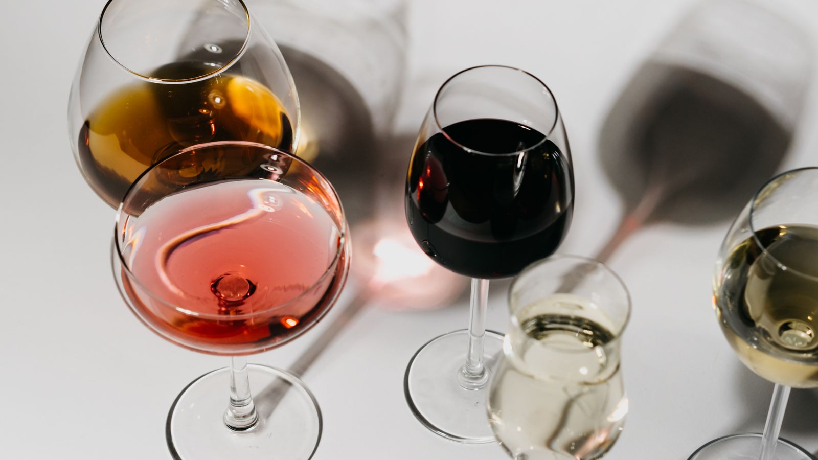 A row of wine glasses in different shapes holding red, white and sparkling wine on a white table