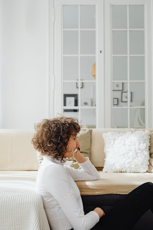 A Side View of a Woman in White Long Sleeves Sitting Near the Couch
