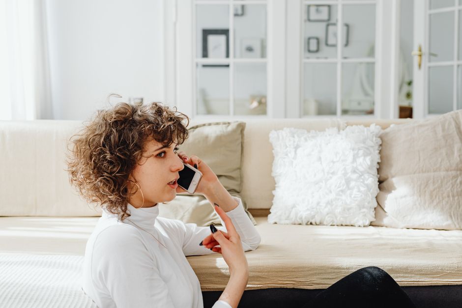 A woman is seated, talking on her phone in a bright, cozy living room.