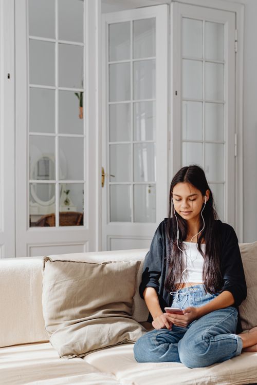 Free Young woman listening to music on earphones while sitting at home, enjoying a relaxing moment. Stock Photo