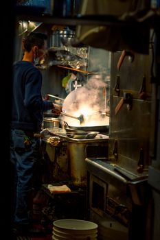 A chef cooks in an industrial kitchen with steam and warm lighting, creating an atmospheric scene.