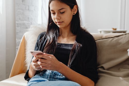 Free A young woman sitting on a couch using her smartphone in a cozy indoor setting. Stock Photo