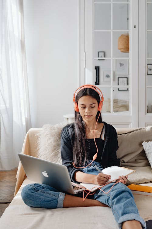 Woman Writing on a Notebook While Using Laptop