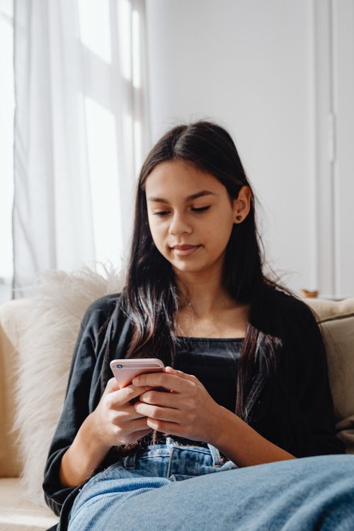 Free Young woman sitting on a couch using a smartphone, relaxed and casual. Stock Photo