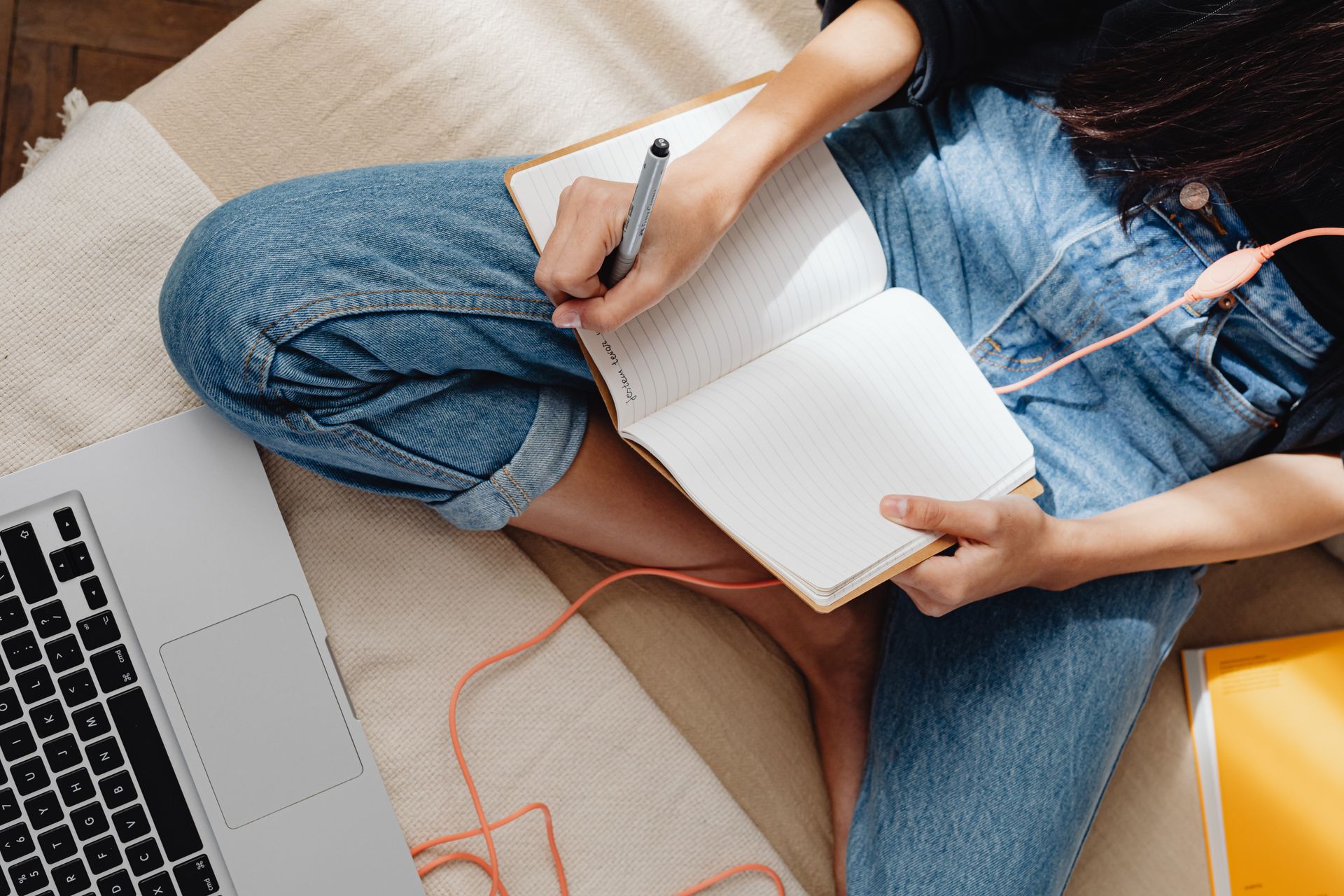 Close-up of a person writing in a notebook next to a laptop indoors.