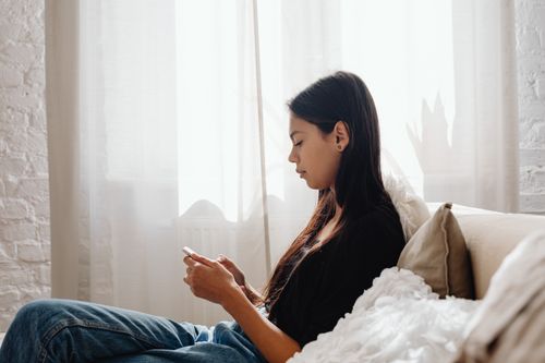 Free A teenager sits comfortably on a couch, focused on her smartphone in a peaceful indoor setting. Stock Photo
