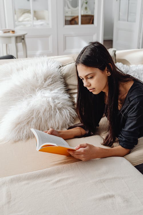 Free Woman Reading a Book While Lying on Sofa Stock Photo