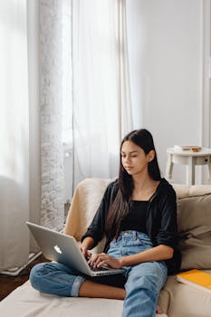 Young woman sitting on sofa using laptop at home for online study