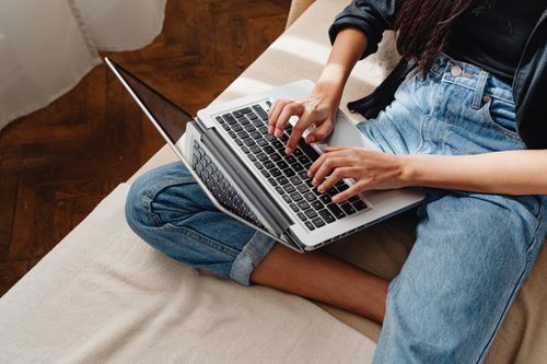 Free Close-up of a woman typing on a laptop, sitting cross-legged indoors. Stock Photo